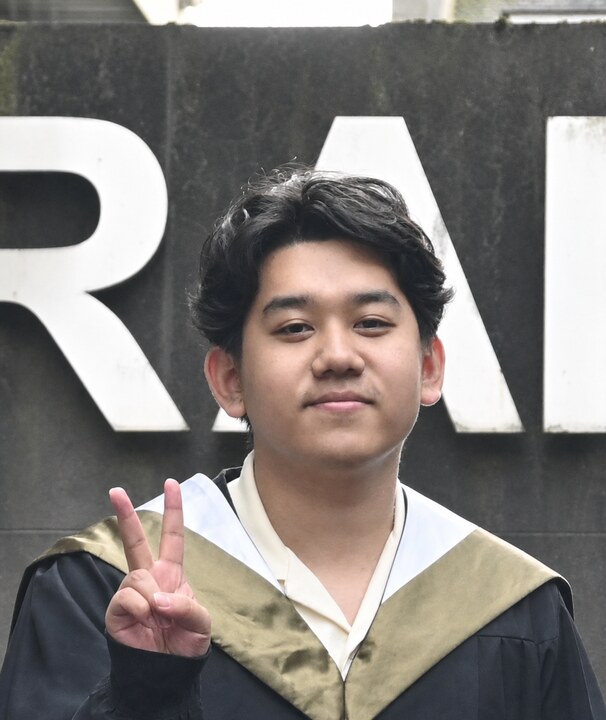 Portrait of Fuyan Zhang in graduation attire, making a V sign